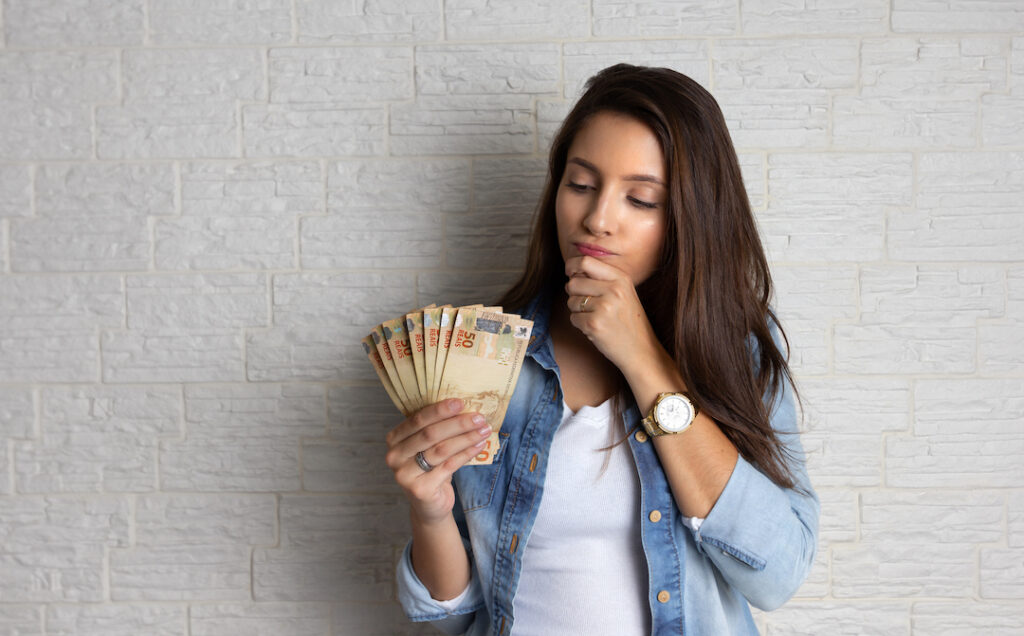 mujer joven con dinero en la mano pensando en qué invertir